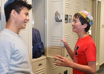 Two Jewish middle school boys standing at an open locker smiling